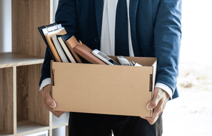 pessoa de paletó segurando uma caixa com diversos objetos pessoais dentro.