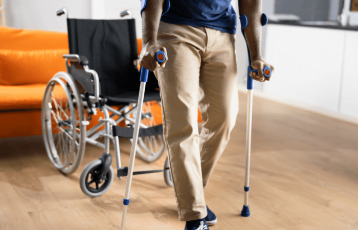 pessoa em pé de moletas e uma cadeira de rodas atrás