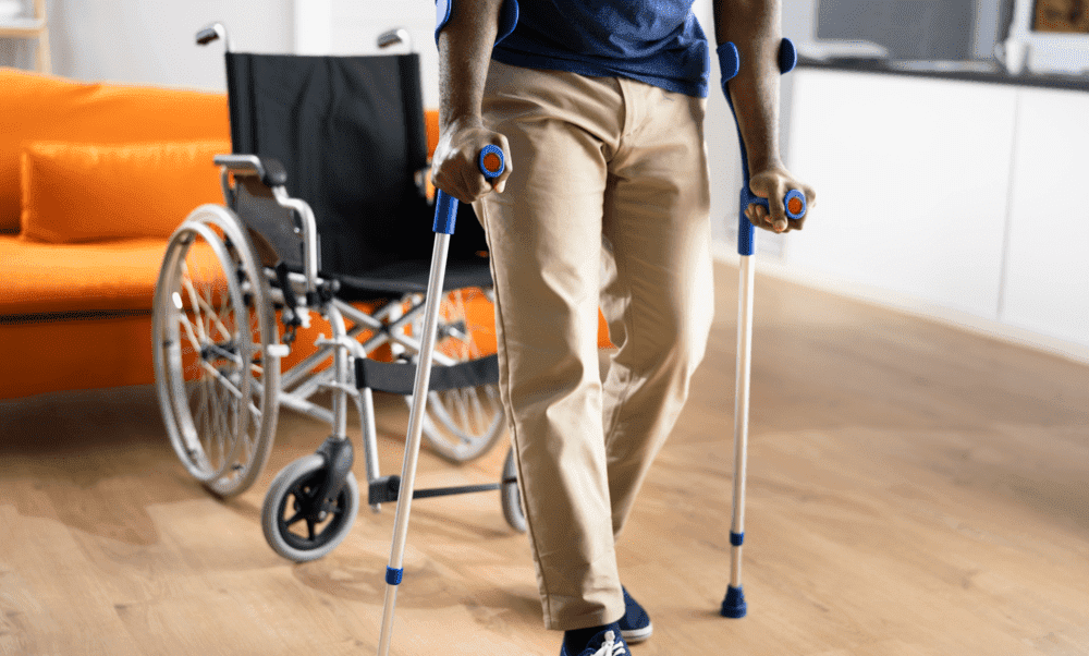 pessoa em pé de moletas e uma cadeira de rodas atrás